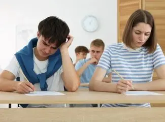 two students i.e. boy and girl writing the exam. boy wearing a white t shirt and the blue sweater wrapped around the neck looks little anxious and the girl is writing silently.